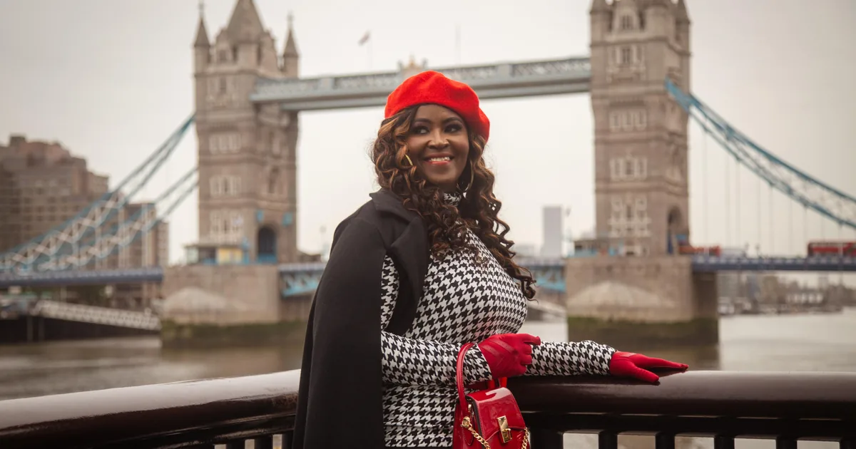 A woman in a red hat and gloves posing on the riverside railings in front of Tower Bridge